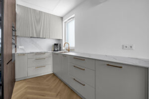 Dolne szafki kuchenne na wymiar z lakierowanymi frontami i złotymi uchwytami.