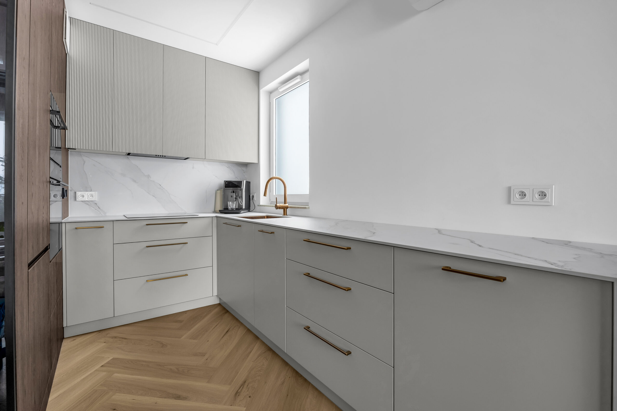 Dolne szafki kuchenne na wymiar z lakierowanymi frontami i złotymi uchwytami.