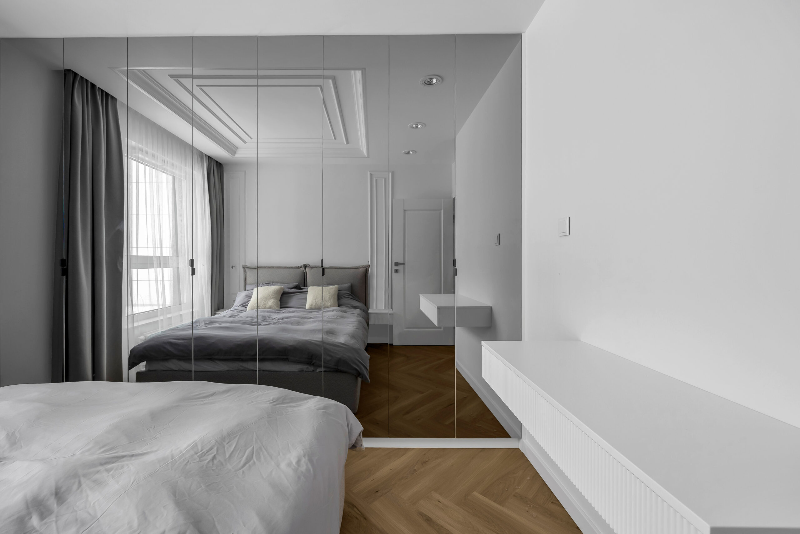 Szafa na wymiar w sypialni z lustrzanymi frontami umieszczona naprzeciwko łóżka.