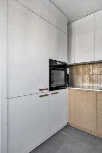 Kuchnia na wymiar z białymi frontami w słupku i szafkach wiszących oraz drewnianymi szafkami dolnymi.