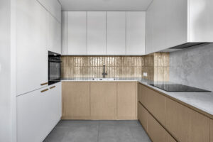 Kuchnia z płytkami między szafkami oraz białymi i drewnianymi frontami.